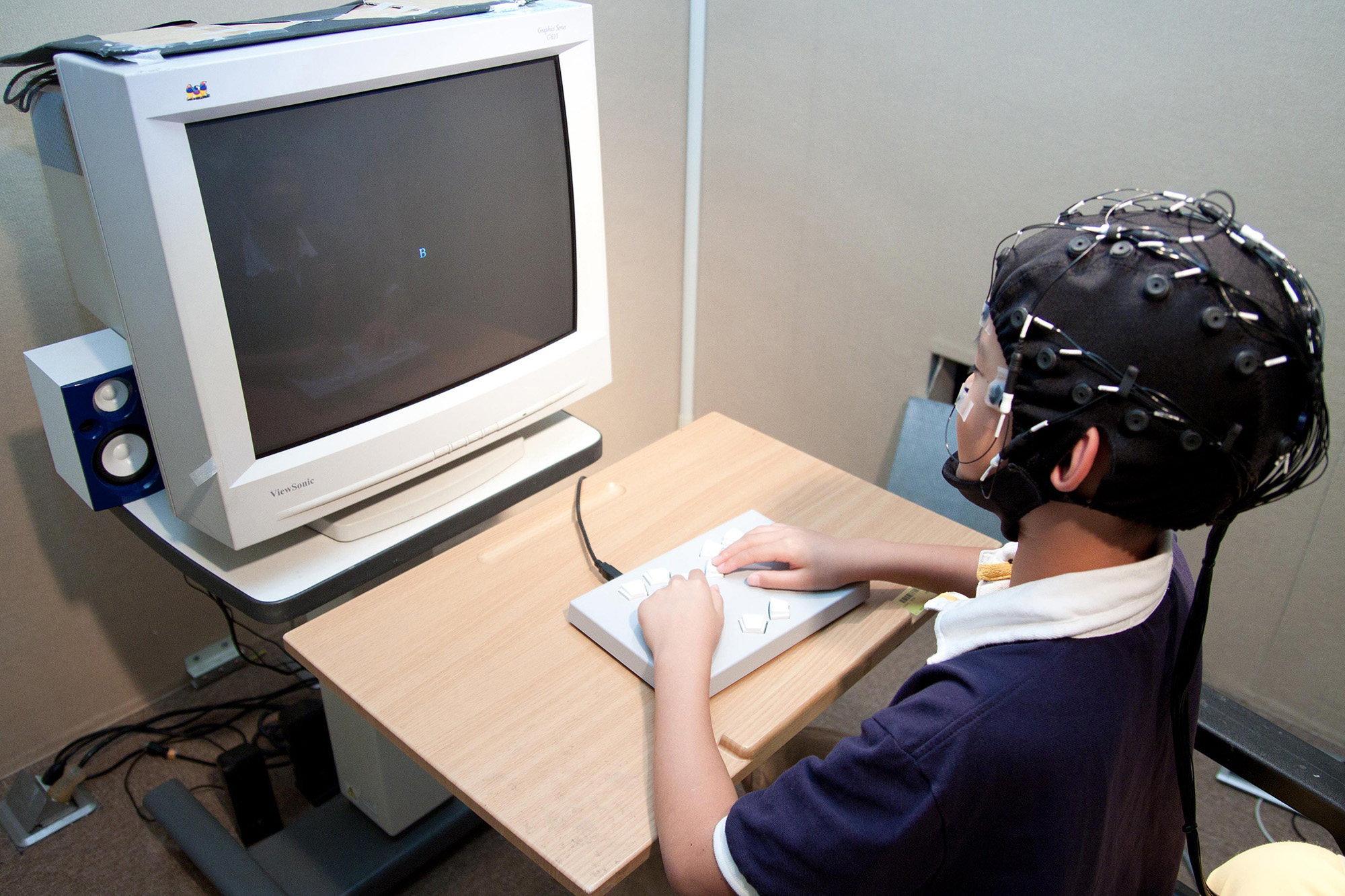 受試者戴著腦波實驗專用帽，看著電腦螢幕按按鍵、或是玩遊戲，藉此收集大腦的反應數據。 圖片來源│大腦與語言實驗室